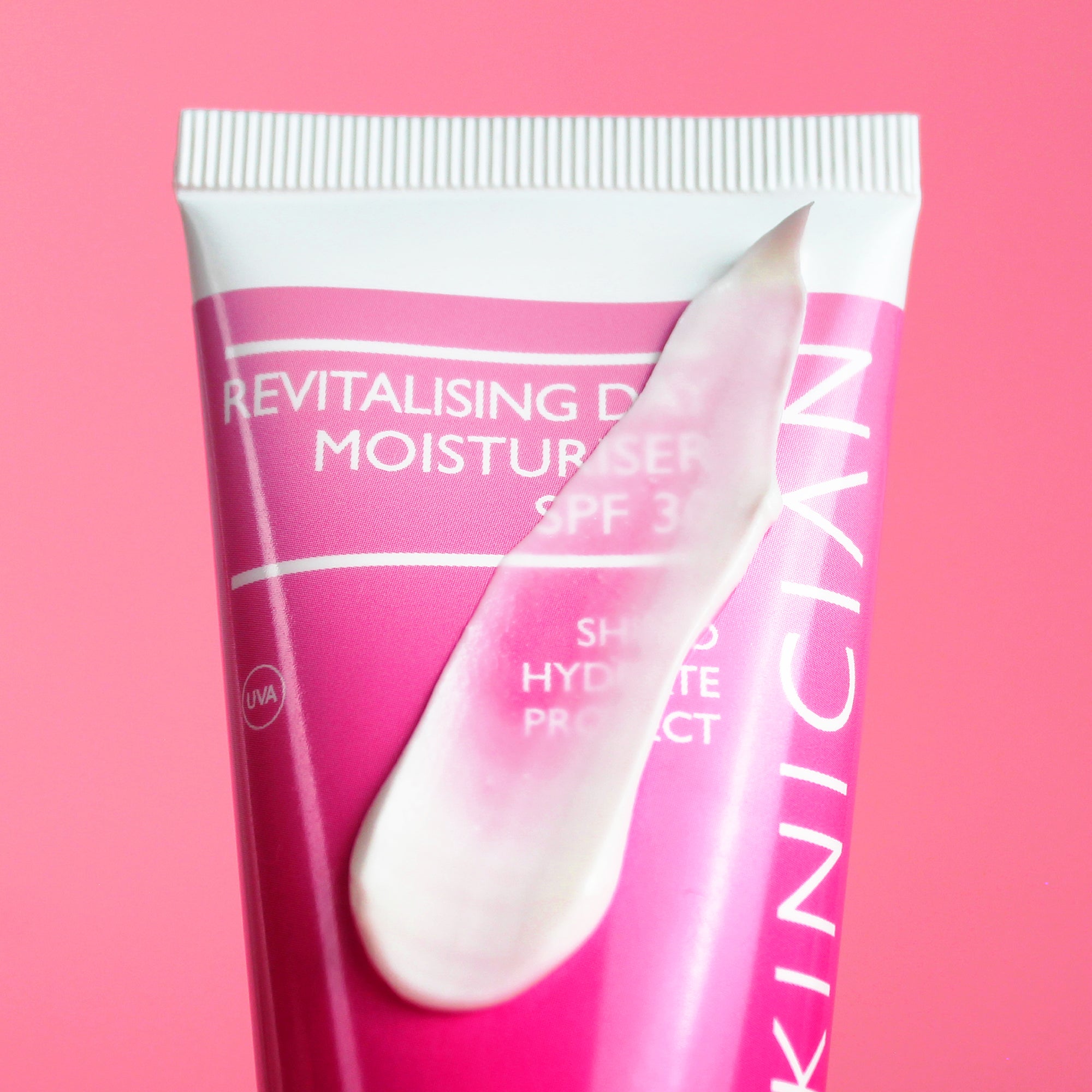 Image of Skinician Revitalising Day Moisturiser tube on a pink background with the product texture swiped across the bottle to demonstrate the creamy texture of the moisturiser.