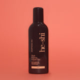 Bottle of he-shi Dark Express Liquid Tan on a coral background