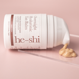 He-shi Overnight Hyaluronic Tan Balm laying on its side with the product pouring out to show the creamy texture of the product