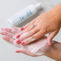 Person applying He-Shi Tan Remover and Primer to hands with the bottle in the background