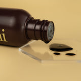 Image of he-shi Express Liquid Tan bottle  on its side with the liquid product spilling onto a glass plinth to show the texture of the product 