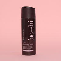 He-Shi Gold Tanning Milk bottle on pink background