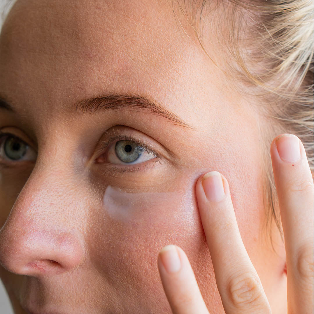 Close-up of a person applying cream under their eye with a finger.