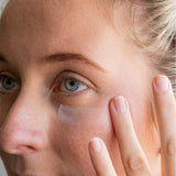 Close-up of a person applying cream under their eye with a finger.
