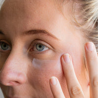 Close-up of a person applying cream under their eye with a finger.
