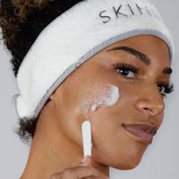 Woman applying Cleansing Balm to her check using a spatula to demonstrate the balm texture of the product
